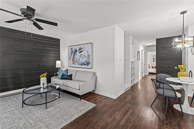 living area with ceiling fan with notable chandelier, an accent wall, wood finished floors, and baseboards