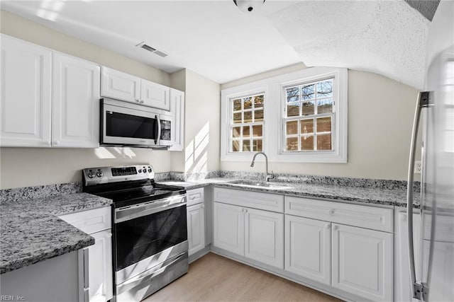 kitchen featuring a sink, visible vents, white cabinets, appliances with stainless steel finishes, and light wood finished floors