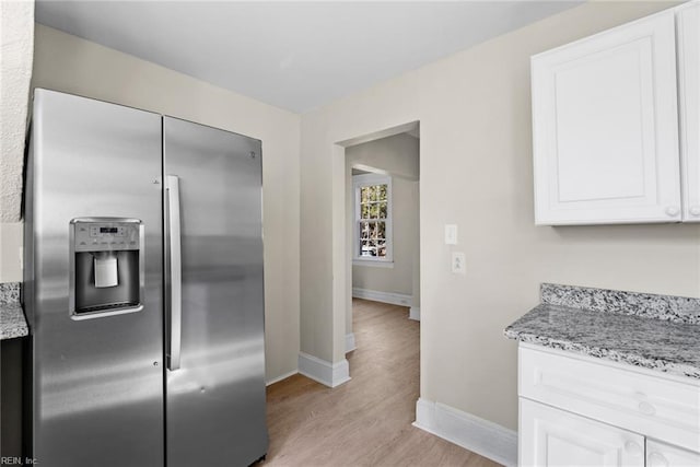 kitchen with light wood-style floors, white cabinets, light stone countertops, stainless steel fridge, and baseboards