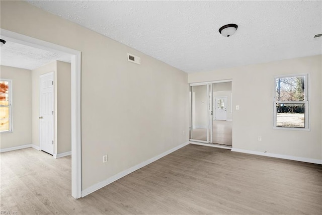 unfurnished room featuring a textured ceiling, light wood finished floors, visible vents, and baseboards