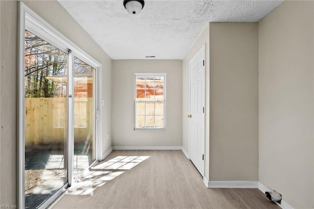 unfurnished room with baseboards, a textured ceiling, visible vents, and light wood-style floors