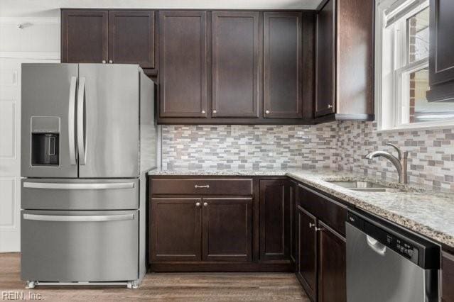 kitchen featuring light stone counters, stainless steel appliances, decorative backsplash, dark brown cabinetry, and a sink