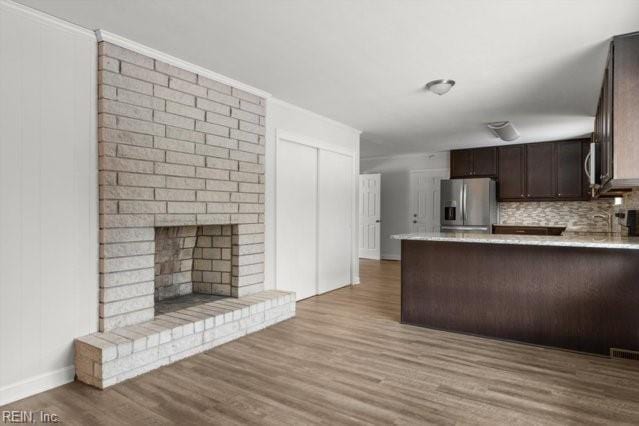 kitchen with light countertops, light wood-style flooring, a brick fireplace, dark brown cabinetry, and stainless steel fridge