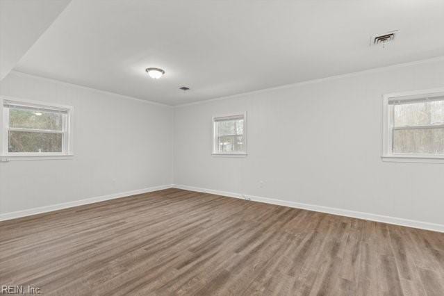 empty room featuring a wealth of natural light, ornamental molding, and wood finished floors