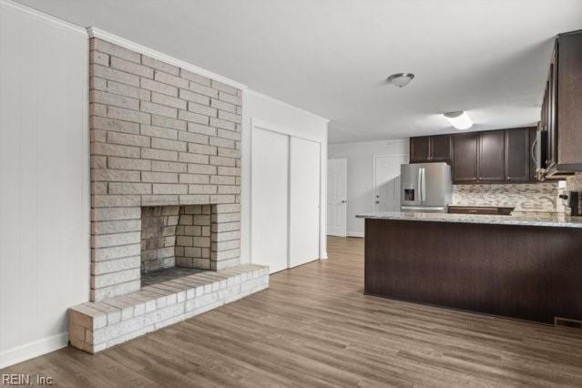 kitchen featuring light wood-style flooring, a fireplace, dark brown cabinets, backsplash, and stainless steel fridge