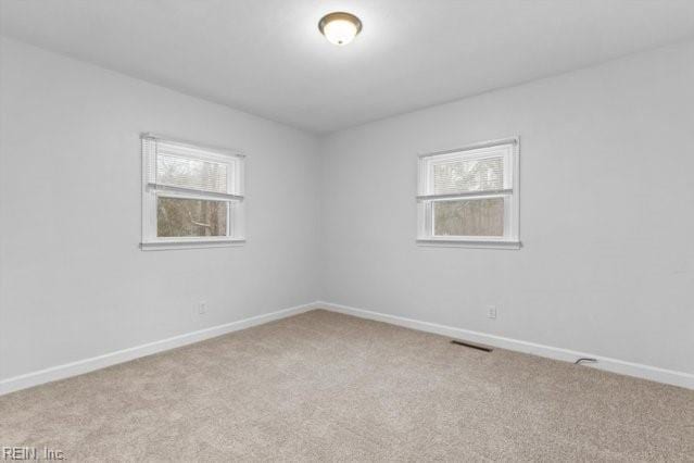 empty room featuring light colored carpet, visible vents, and baseboards