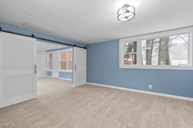 empty room with light colored carpet, baseboards, and a barn door