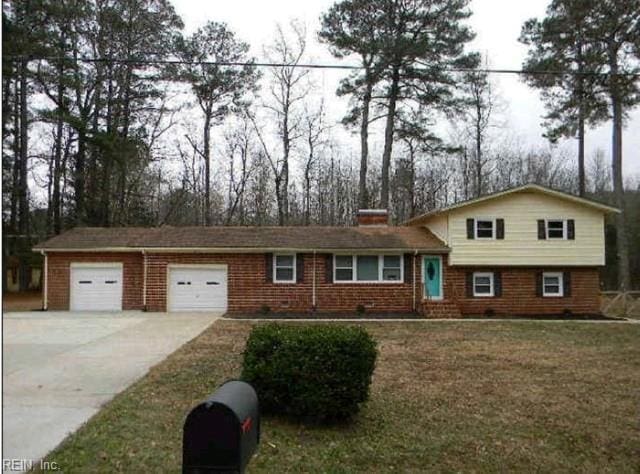 tri-level home with a garage, driveway, a chimney, a front lawn, and brick siding