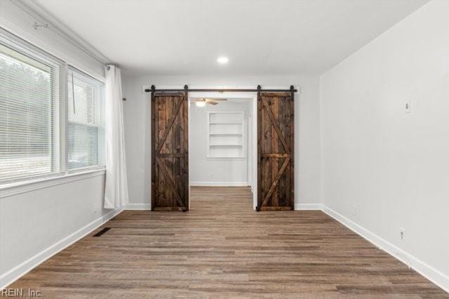 unfurnished room with a barn door, wood finished floors, visible vents, built in features, and baseboards