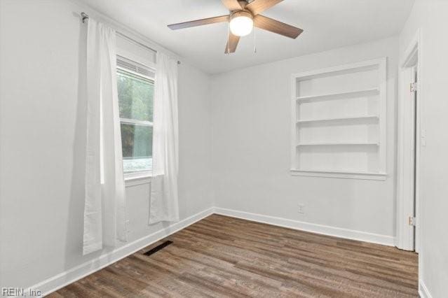 empty room featuring ceiling fan, dark wood-style flooring, visible vents, built in features, and baseboards