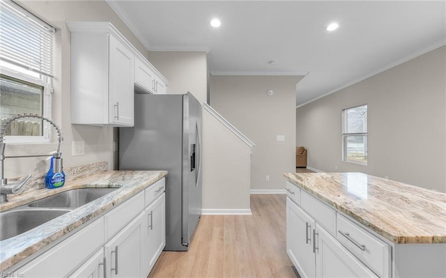 kitchen with stainless steel fridge, ornamental molding, light wood-type flooring, white cabinetry, and a sink