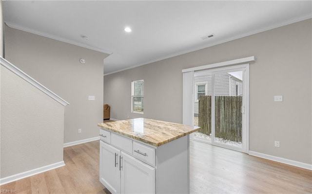 kitchen with visible vents, ornamental molding, white cabinets, a kitchen island, and light stone countertops