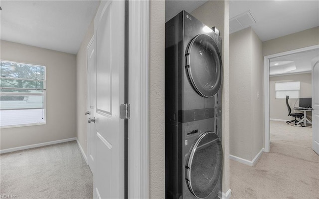 laundry area with baseboards, stacked washer and dryer, laundry area, and light colored carpet