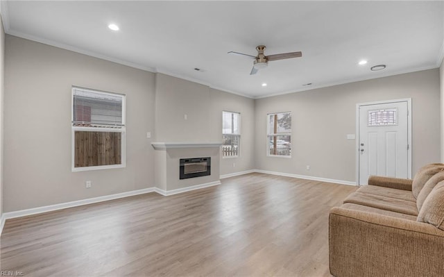 living area with light wood-style flooring, recessed lighting, baseboards, a glass covered fireplace, and crown molding