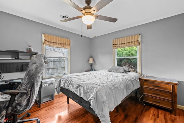 bedroom with ceiling fan, wood finished floors, visible vents, and baseboards