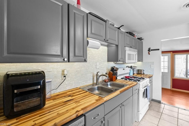 kitchen featuring light tile patterned flooring, gray cabinetry, white appliances, a sink, and tasteful backsplash