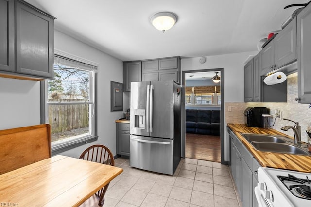 kitchen with white gas stove, stainless steel refrigerator with ice dispenser, a sink, and gray cabinetry