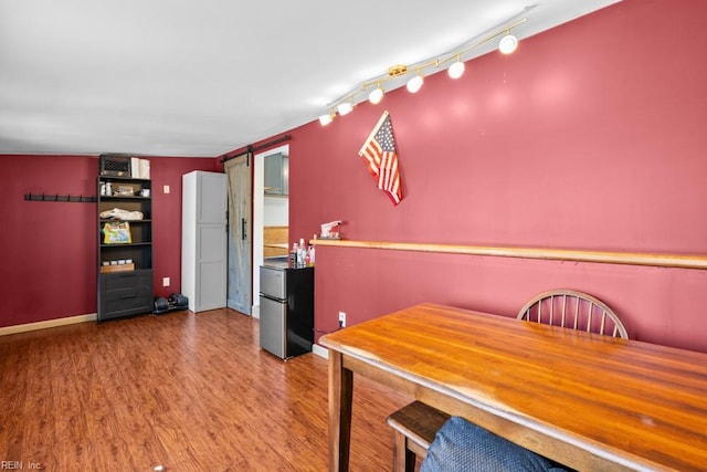 unfurnished dining area featuring rail lighting, a barn door, baseboards, and wood finished floors