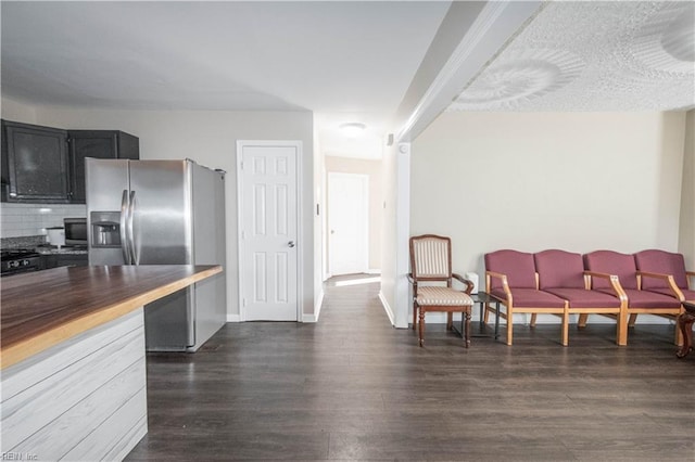 kitchen with dark wood-style floors, wooden counters, decorative backsplash, stainless steel fridge, and baseboards