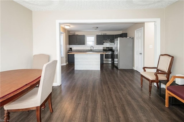 kitchen featuring dark wood-style flooring, light countertops, decorative backsplash, appliances with stainless steel finishes, and under cabinet range hood