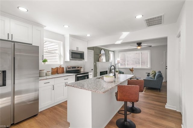 kitchen with a breakfast bar, visible vents, appliances with stainless steel finishes, white cabinets, and a sink