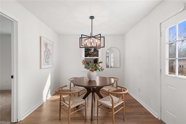 dining room featuring a healthy amount of sunlight, dark wood finished floors, baseboards, and an inviting chandelier