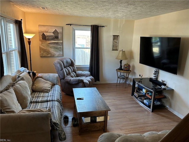 living area featuring visible vents, baseboards, a textured ceiling, and wood finished floors