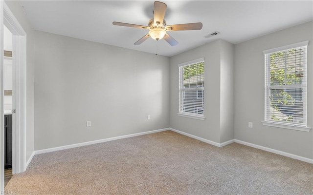 unfurnished room with a ceiling fan, light colored carpet, visible vents, and baseboards