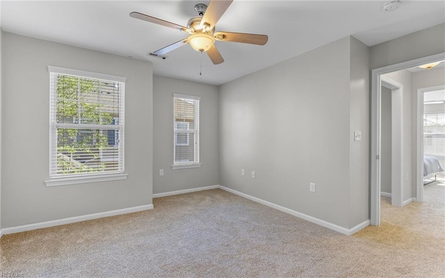 spare room with light colored carpet, ceiling fan, and baseboards