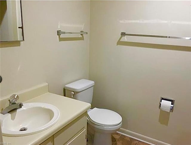 half bathroom featuring toilet, baseboards, and vanity