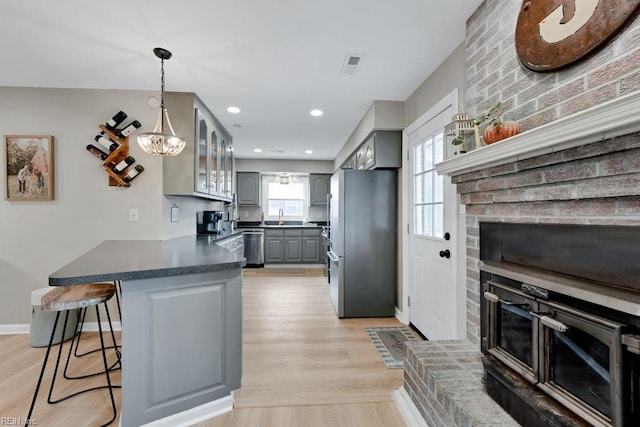 kitchen featuring dark countertops, gray cabinetry, appliances with stainless steel finishes, glass insert cabinets, and a kitchen breakfast bar