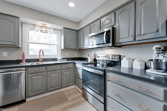 kitchen with a sink, appliances with stainless steel finishes, dark countertops, and gray cabinets