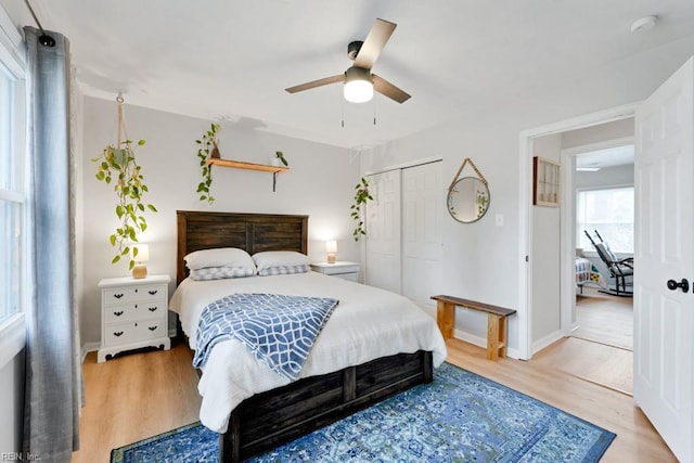 bedroom with light wood-type flooring, ceiling fan, baseboards, and a closet