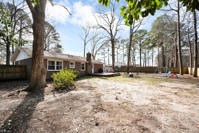 rear view of house with a deck, a playground, a fenced backyard, brick siding, and a chimney