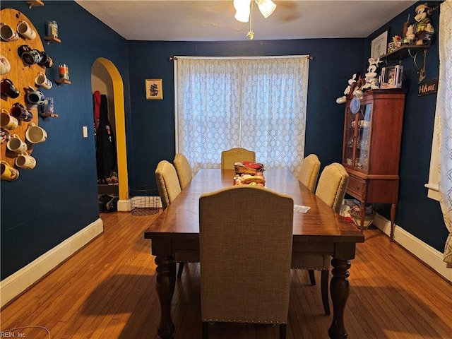 dining space with arched walkways, baseboards, and hardwood / wood-style floors