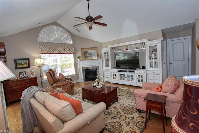 living room featuring lofted ceiling, light wood-style floors, a fireplace, and a ceiling fan