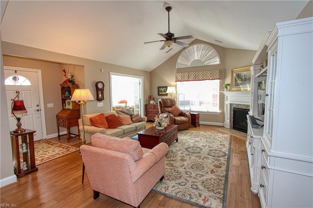 living area featuring lofted ceiling, light wood finished floors, a fireplace, and a ceiling fan