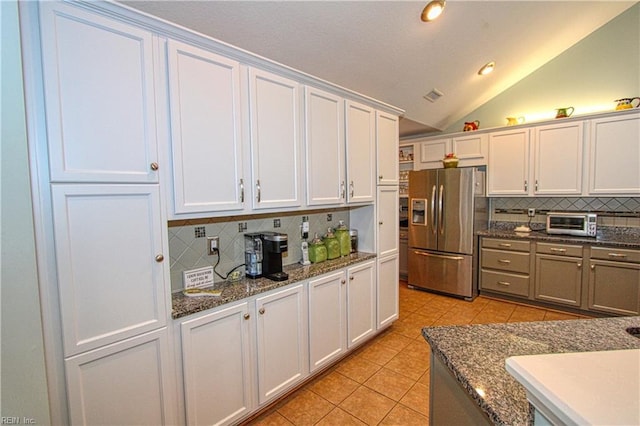 kitchen featuring light tile patterned floors, stainless steel fridge with ice dispenser, vaulted ceiling, white cabinetry, and backsplash