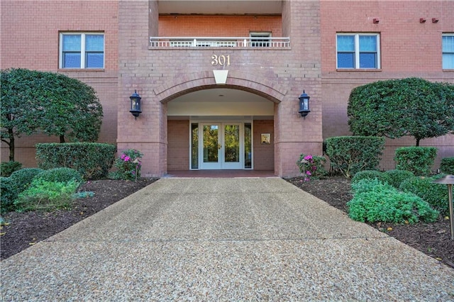 doorway to property with a balcony, brick siding, and french doors