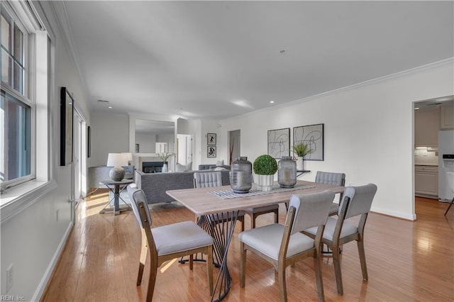 dining area featuring light wood-style flooring, a fireplace, baseboards, and crown molding