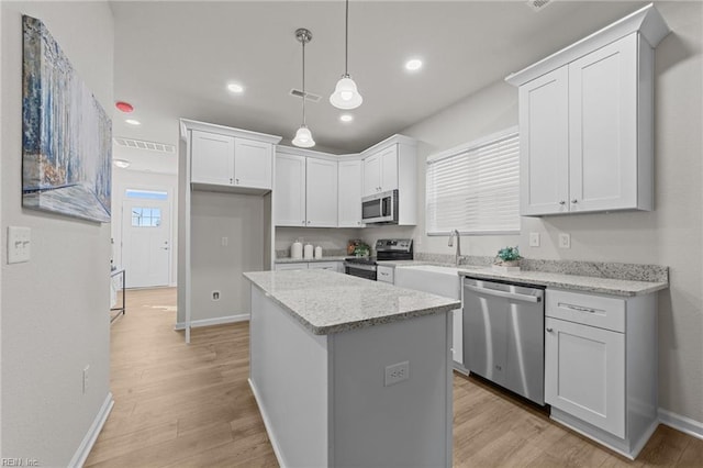 kitchen with white cabinets, a kitchen island, appliances with stainless steel finishes, light stone counters, and hanging light fixtures