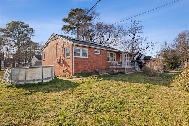 back of property featuring brick siding, a porch, a lawn, crawl space, and an outdoor pool