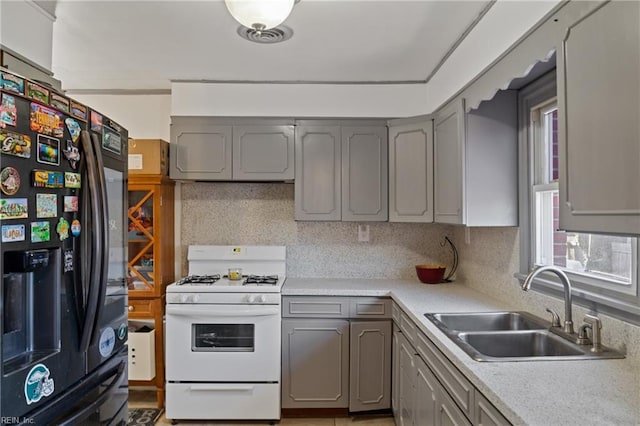 kitchen with black refrigerator with ice dispenser, gray cabinets, a sink, and white range with gas stovetop