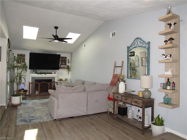 living area with visible vents, lofted ceiling with skylight, ceiling fan, wood finished floors, and a fireplace