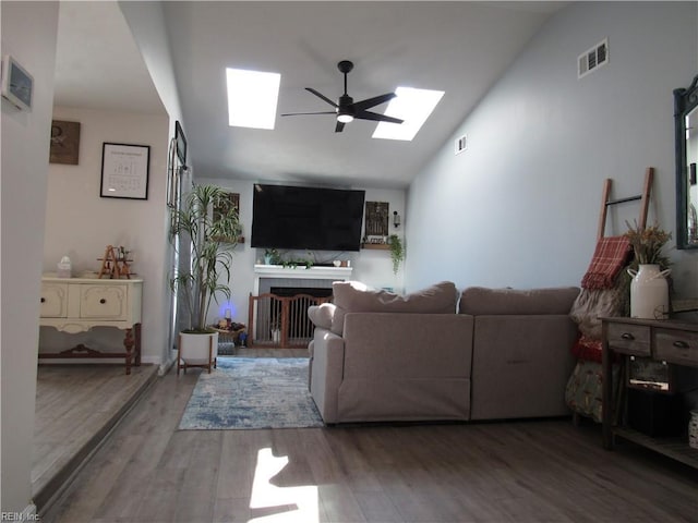 living area with a fireplace, wood finished floors, visible vents, a ceiling fan, and lofted ceiling with skylight