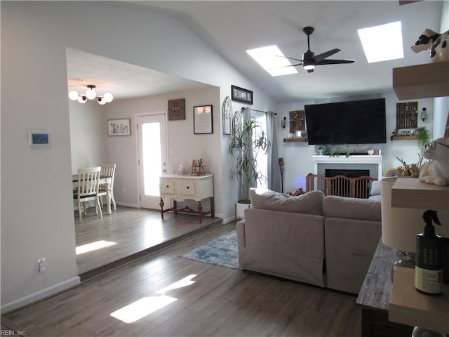 living room featuring ceiling fan with notable chandelier, a fireplace, wood finished floors, baseboards, and lofted ceiling with skylight