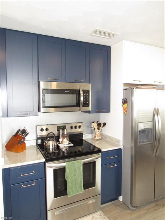 kitchen featuring stainless steel appliances, light wood finished floors, visible vents, and blue cabinets