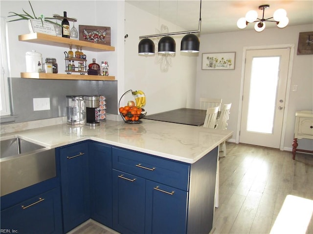 kitchen featuring light wood-style flooring, blue cabinetry, light stone countertops, open shelves, and decorative light fixtures