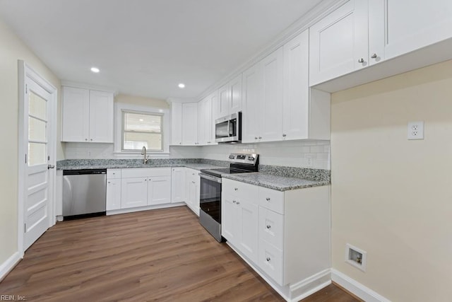 kitchen featuring dark wood-style floors, appliances with stainless steel finishes, light stone countertops, white cabinetry, and a sink