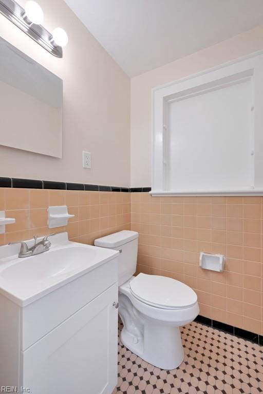 half bath with wainscoting, vanity, toilet, and tile walls